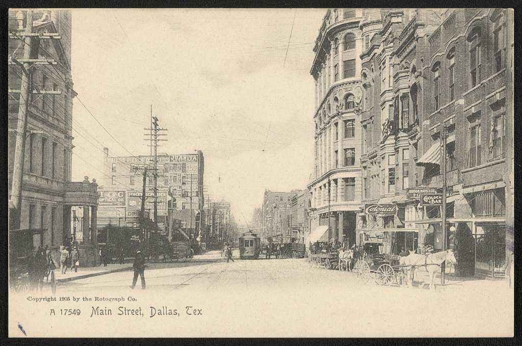 Postcard view down Main Street in Dallas with brick commercial buildings, a streetcar and horse drawn carriages
