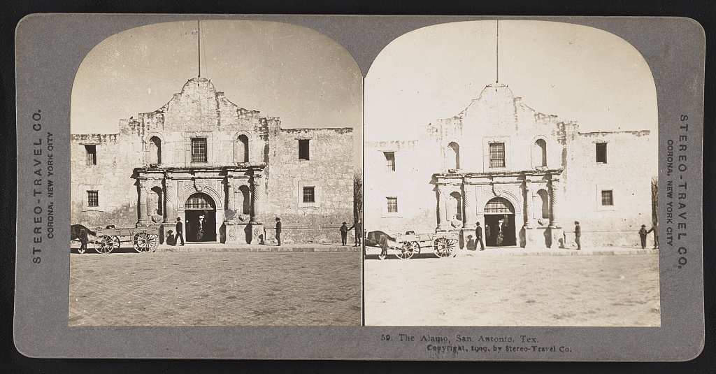 Stereograph card with twin photographs of the stone front of the Alamo chapel, its carved doorway and curved parapet, with a horse and wagon and a few men standing in the street before it.